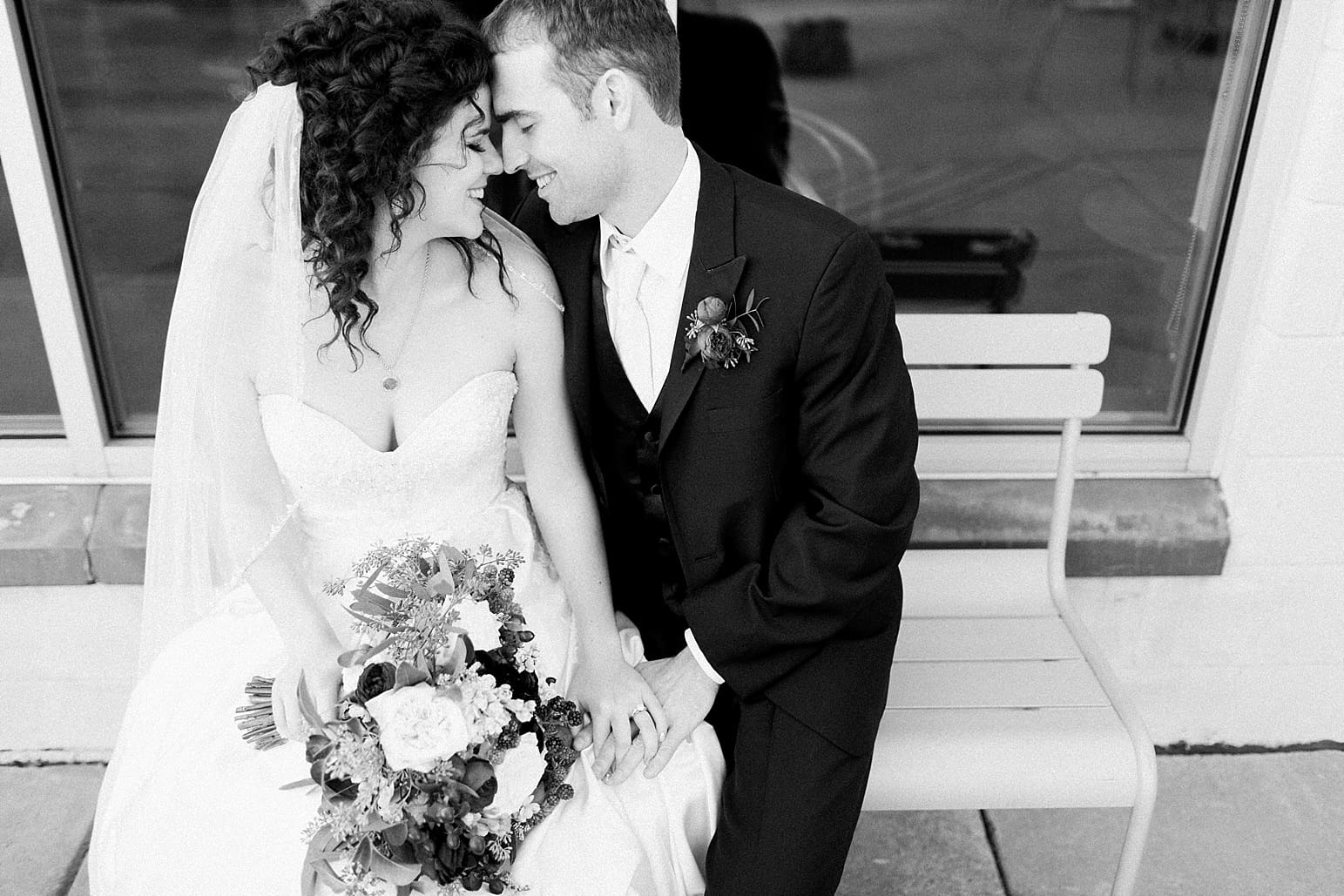 Arielle Peters Photography | Bride and groom sitting on bench outside on wedding day at Baker Street Train Station in Fort Wayne, Indiana.