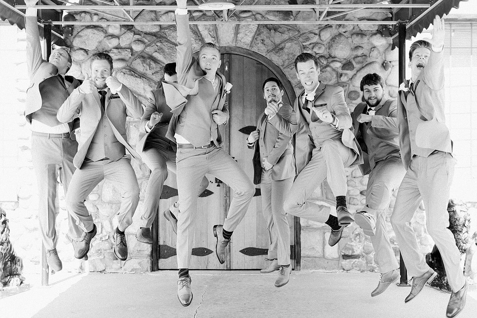 Arielle Peters Photography | Groom and groomsmen jumping next to wooden cellar door on wedding day at Lawton Lions Heritage Community Center in Lawton, Michigan.