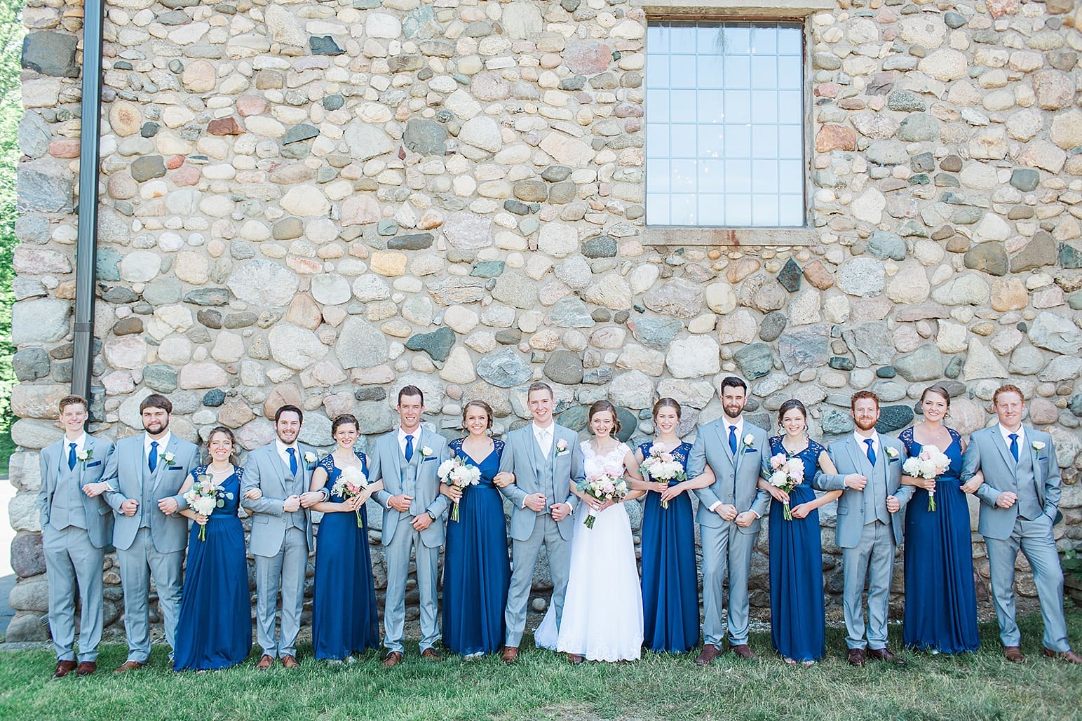 Arielle Peters Photography | Wedding party linking arms next to historic cobblestone building on wedding day at Lawton Lions Heritage Community Center in Lawton, Michigan.