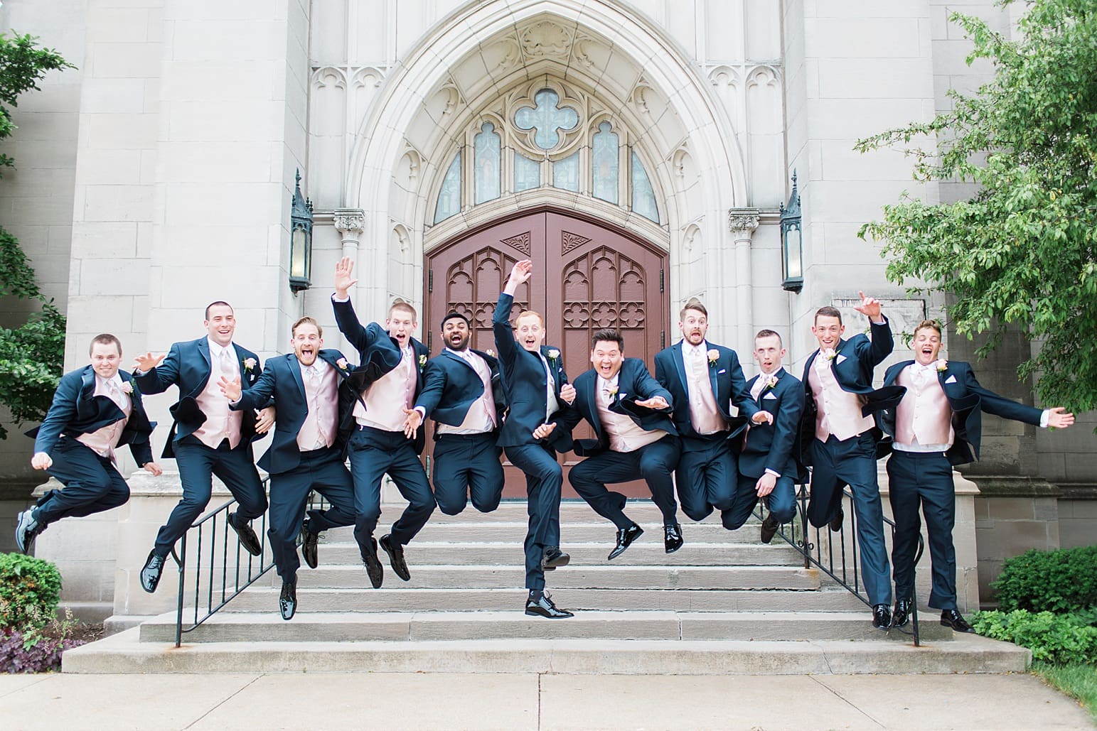 Arielle Peters Photography | Groom and groomsmen jumping outside large cathedral church on wedding day at First United Methodist Church in Mishawaka, Indiana.