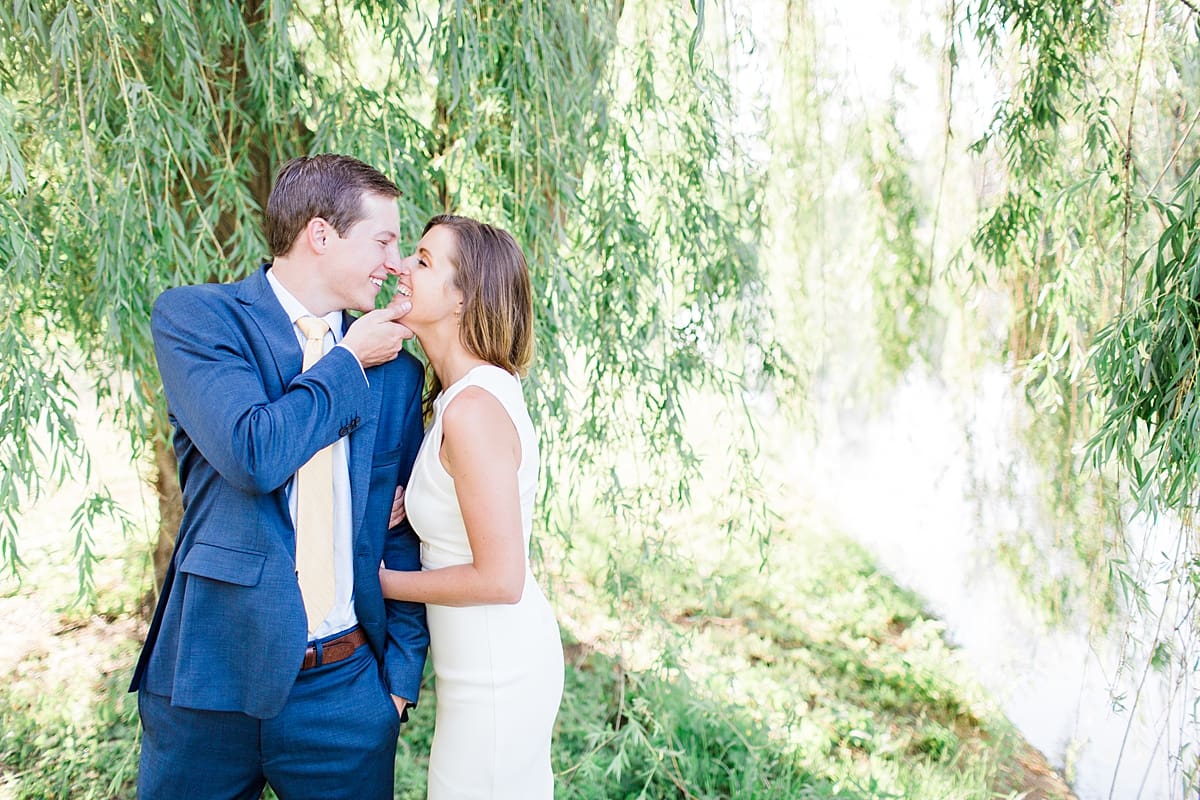 Arielle Peters Photography | Young couple almost kissing under willow tree next to pond taking summer engagement photos.