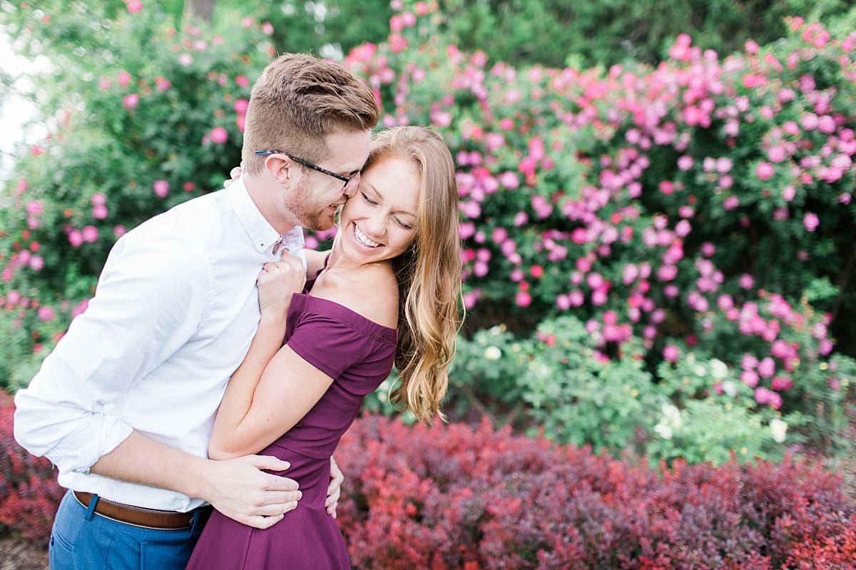 Arielle Peters Photography | Young couple laughing in rose garden taking summer engagement photos.