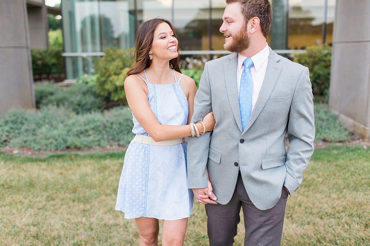 Arielle Peters Photography | Young couple walking next to large glass walls taking summer engagement photos.