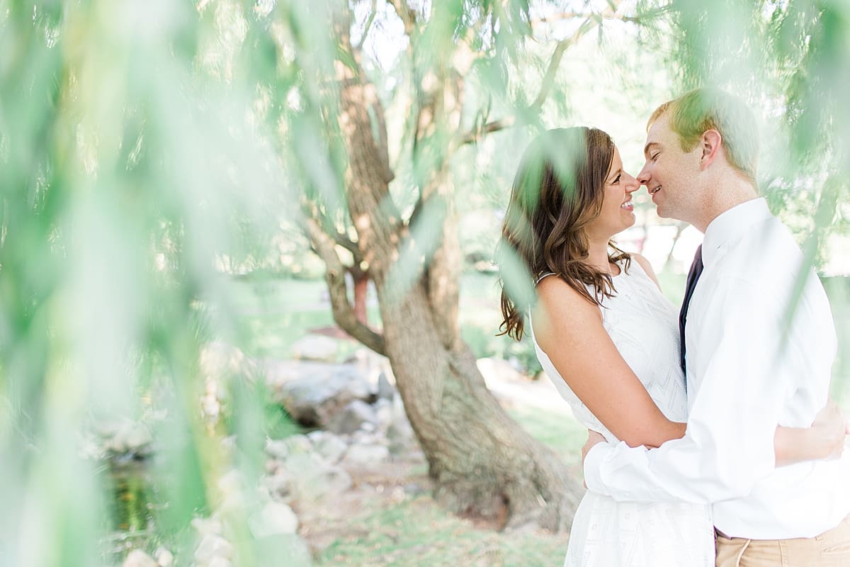 Arielle Peters Photography | Young couple almost kissing under willow tree taking summer engagement photos.