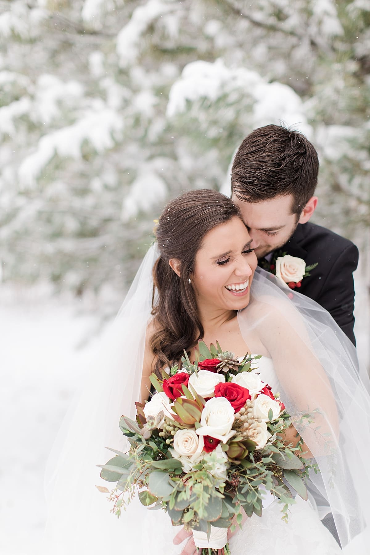 Arielle Peters Photography | Bride and groom hugging in the snow under large pine trees on winter wedding day in Goshen, Indiana.