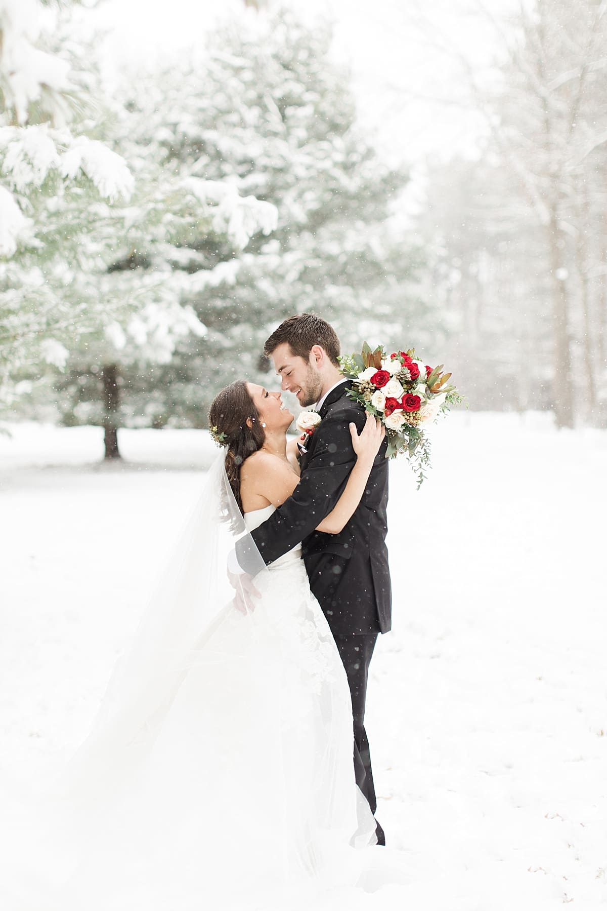 Arielle Peters Photography | Bride and groom hugging outside in the snow under large pine trees on winter wedding day in Goshen, Indiana.