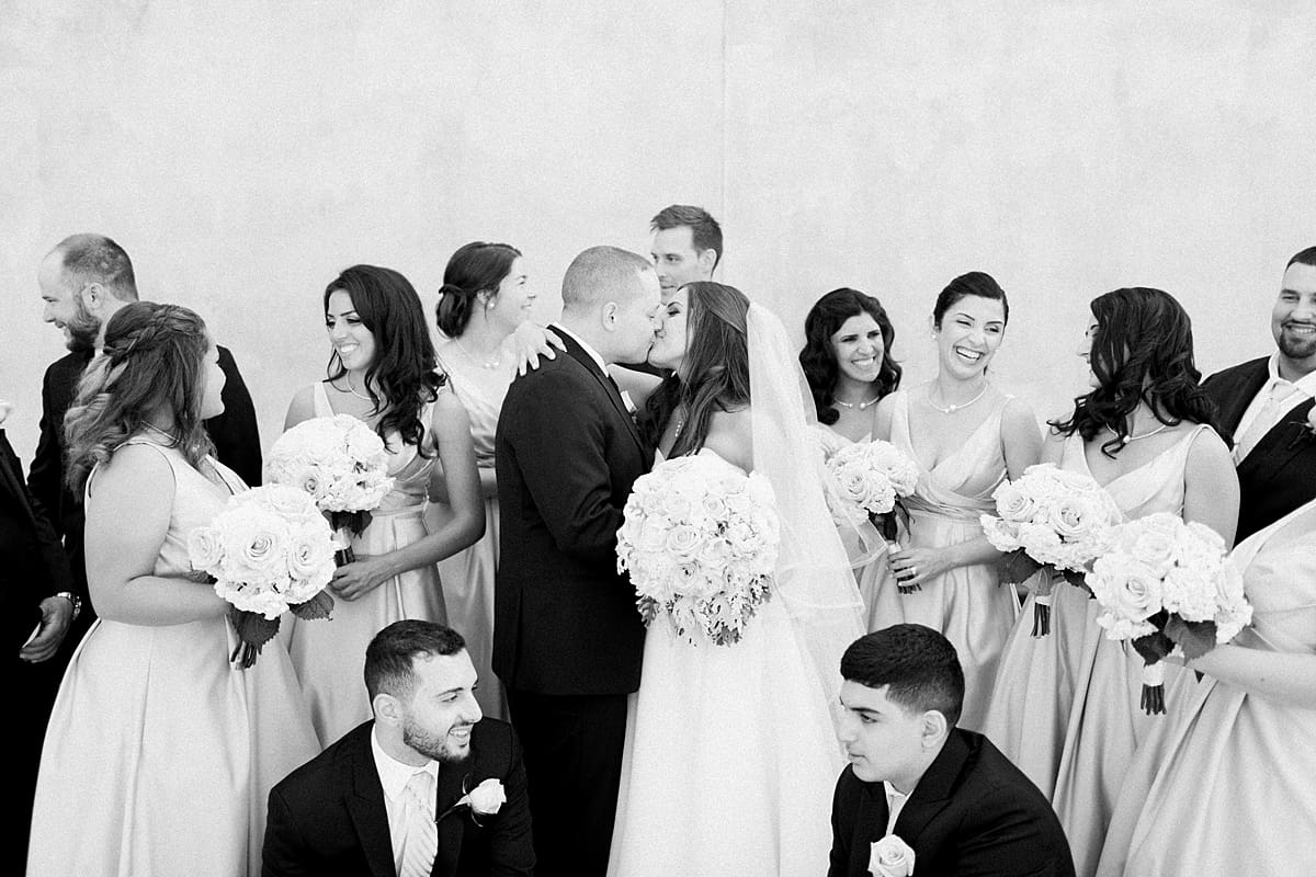 Arielle Peters Photography | Bride and groom kissing with wedding party laughing on summer wedding day at The Inn at Harbor Springs in St. Joseph, Michigan.
