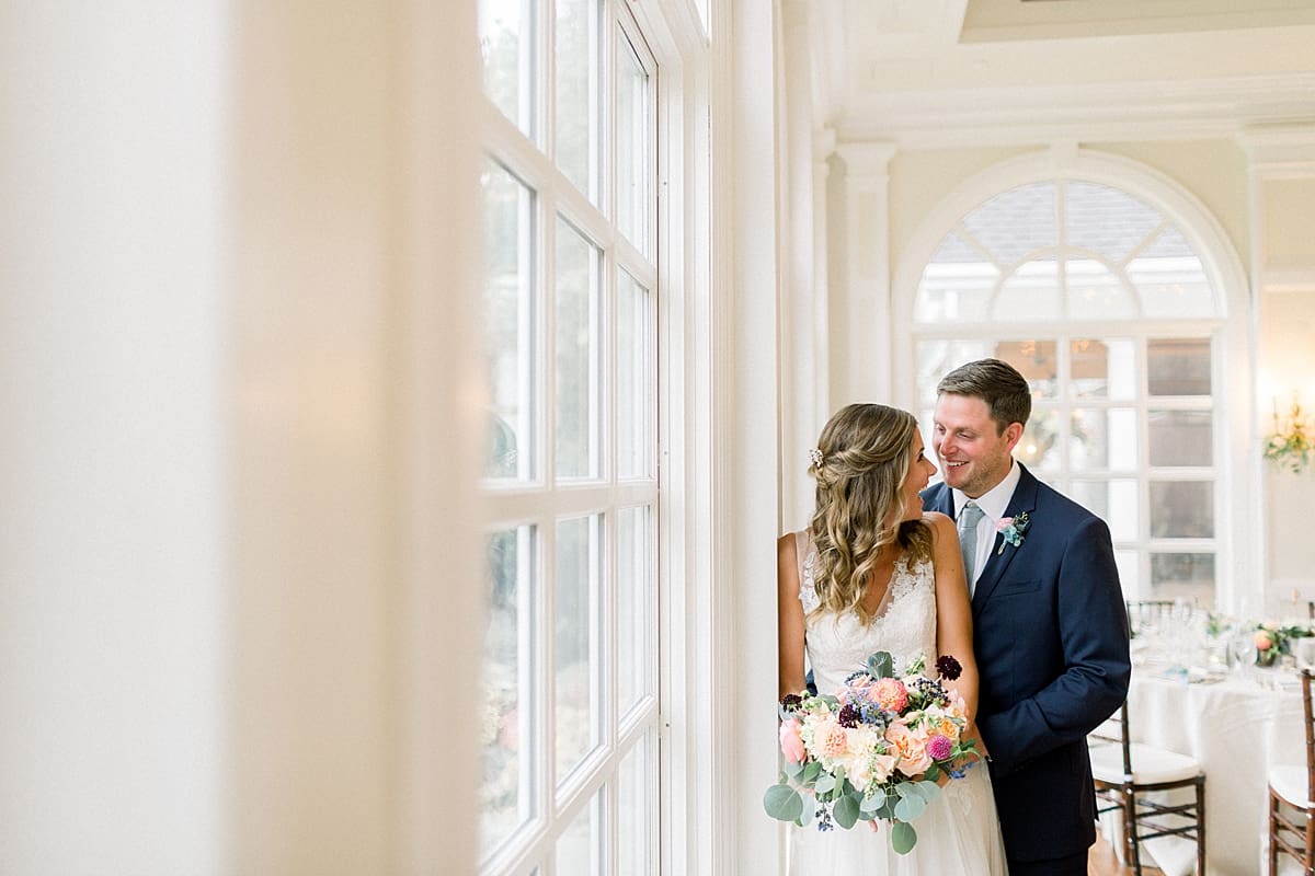 Arielle Peters Photography | Bride and groom laughing by big windows at Sycamore Hills Golf Club in Fort Wayne, Indiana on wedding day.