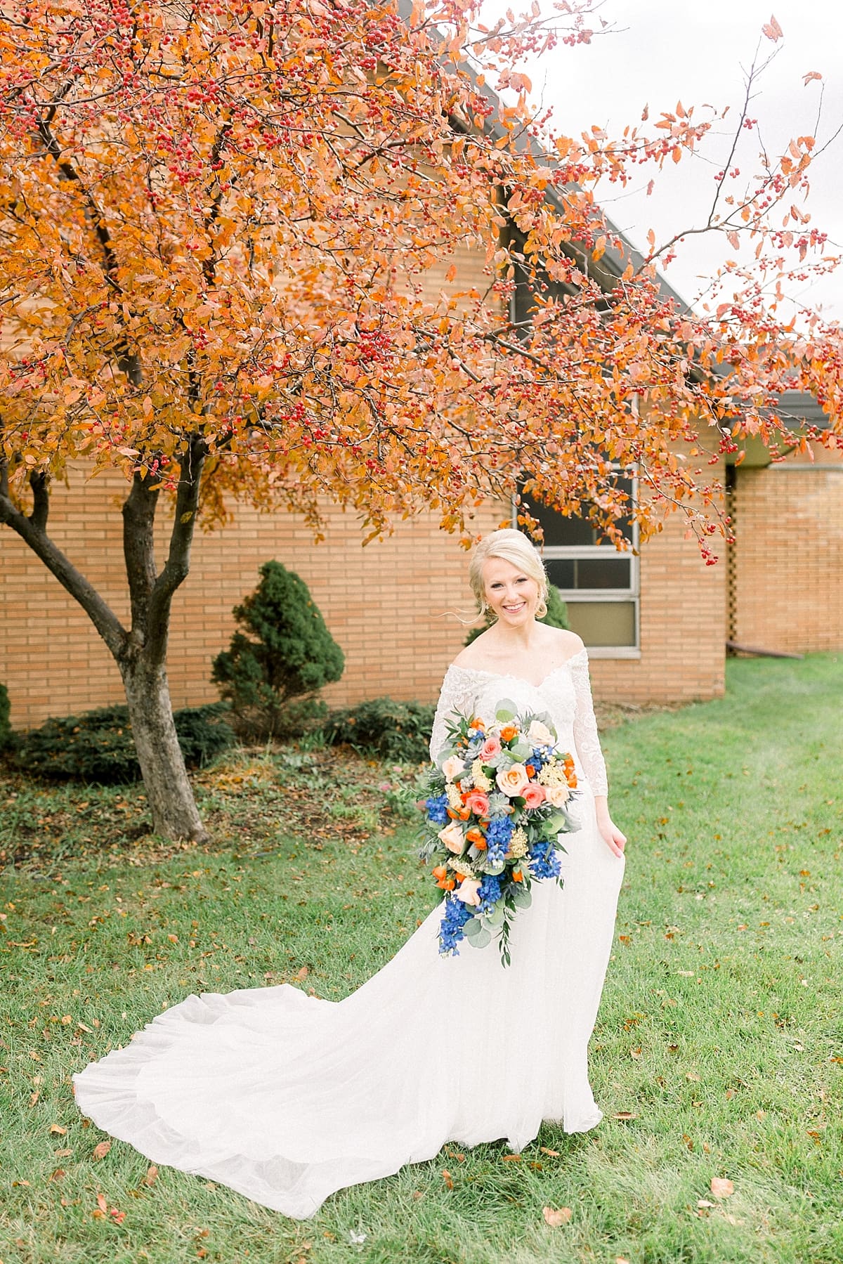 Arielle Peters Photography | Bride smiling with her bouquet outside next to bright orange tree on fall wedding day.