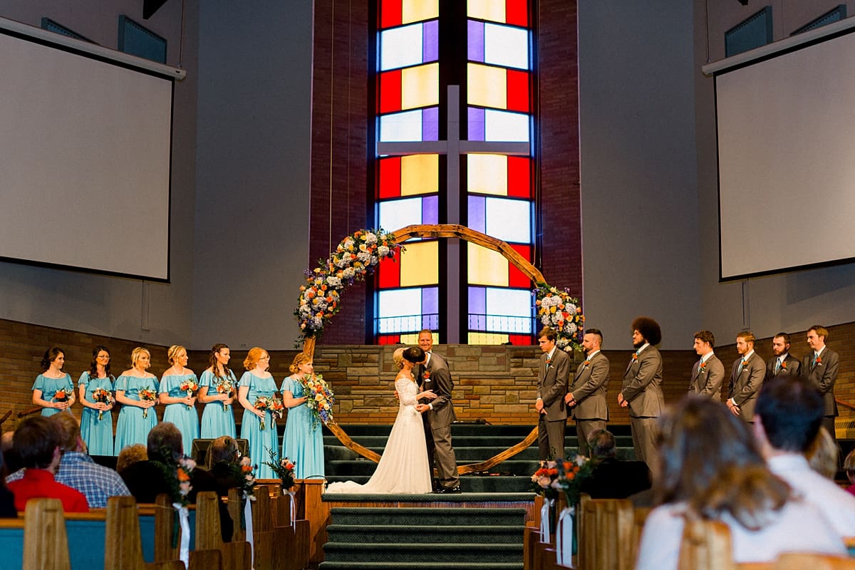 Arielle Peters Photography | Bride and groom kissing at the alter next to stained glass window on their fall wedding day.