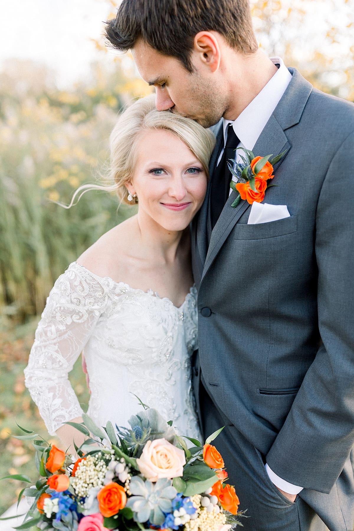 Arielle Peters Photography | Groom kissing the bride's head outside in field on fall wedding day.