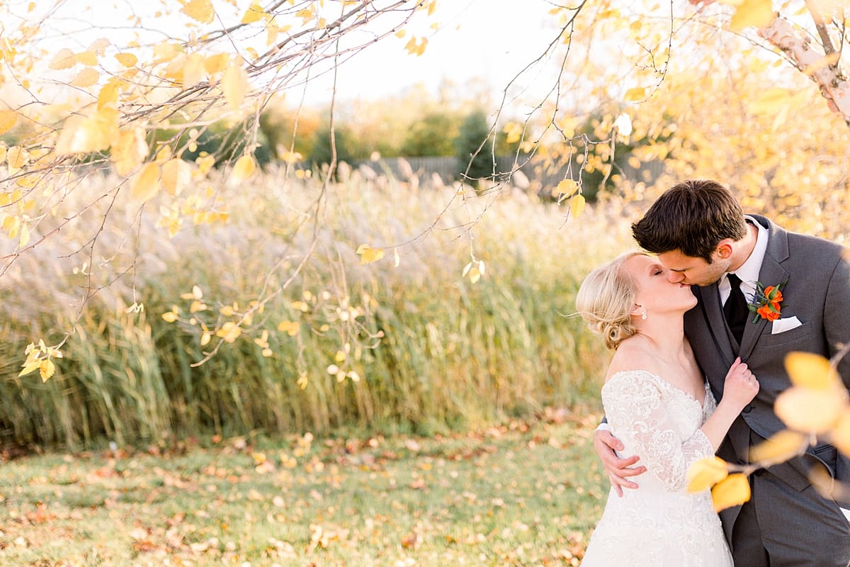 Arielle Peters Photography | Bride and groom kissing in a field next to trees on fall wedding day.
