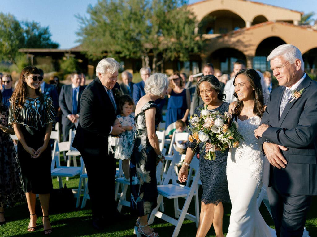 Bride being walked down the aisle by her parents during her Blackstone Country Club wedding ceremony in Peoria