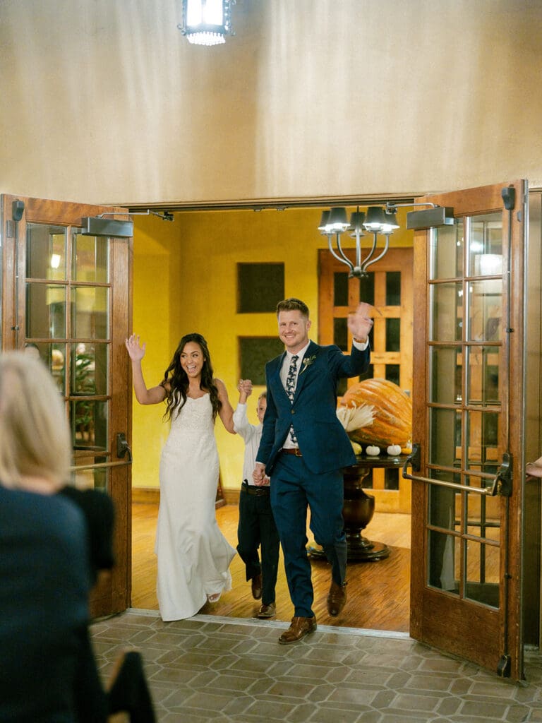 Bride, groom, and their son entering their wedding reception