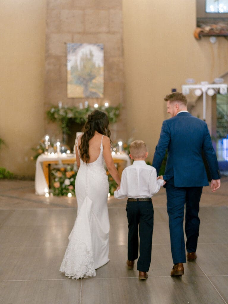 Bride, groom, and their son walking in their wedding reception