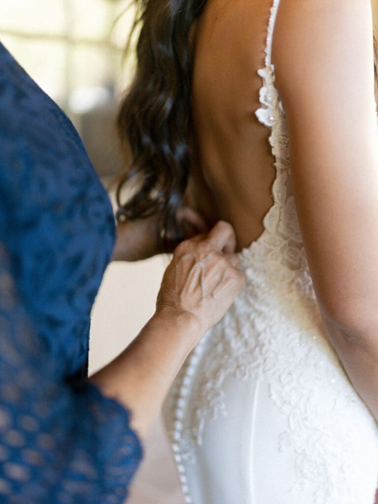 Close up shot of a mother buttoning her daughters wedding dress up. 
