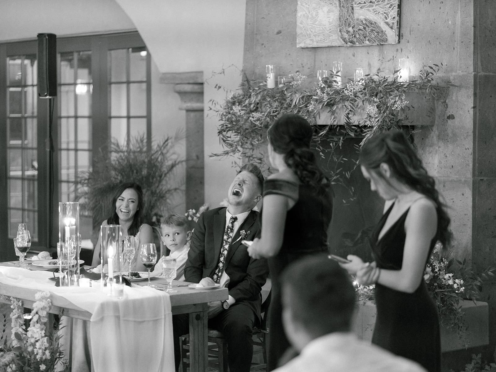 Black and white photo of a bride and groom laughing during wedding toasts