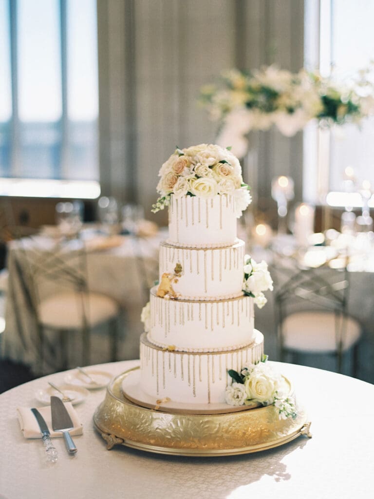 A white 4 tiered cake with white florals and golden accent drippings