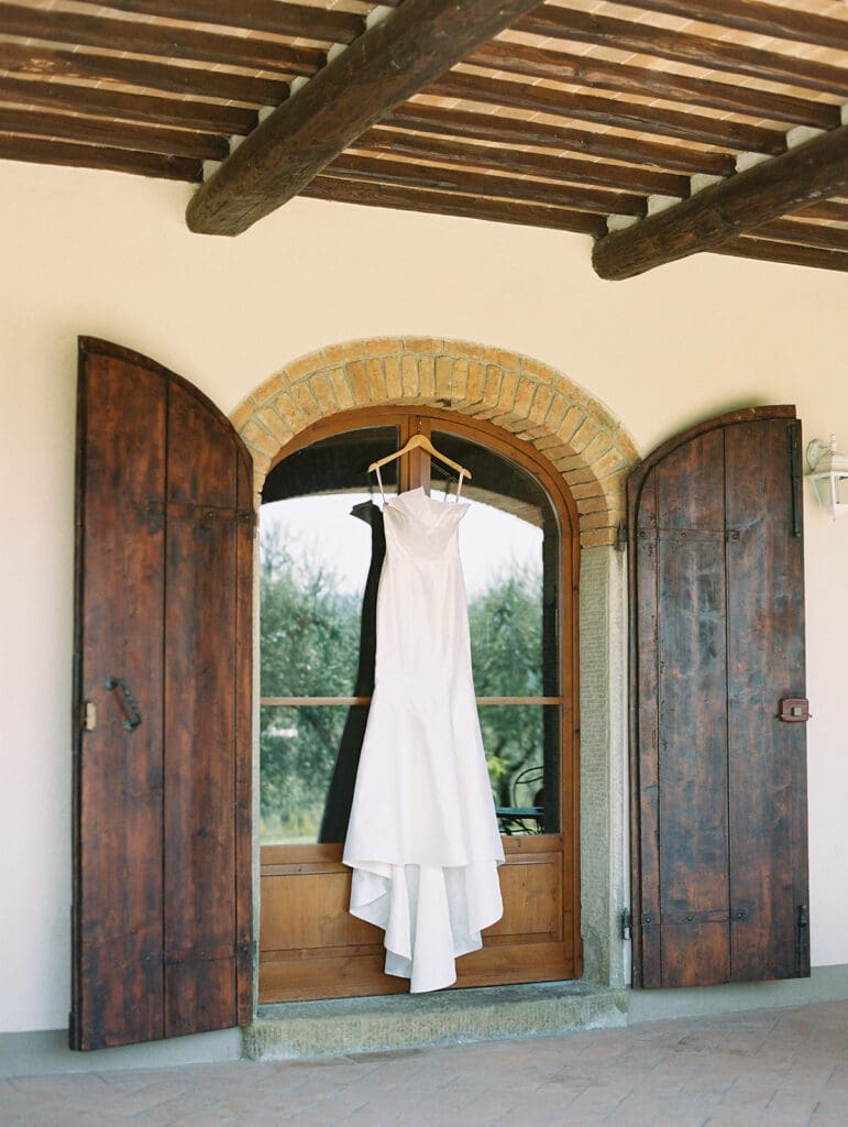 Brides elegant white wedding dress hanging at Villa Petra in Tuscany, Italy