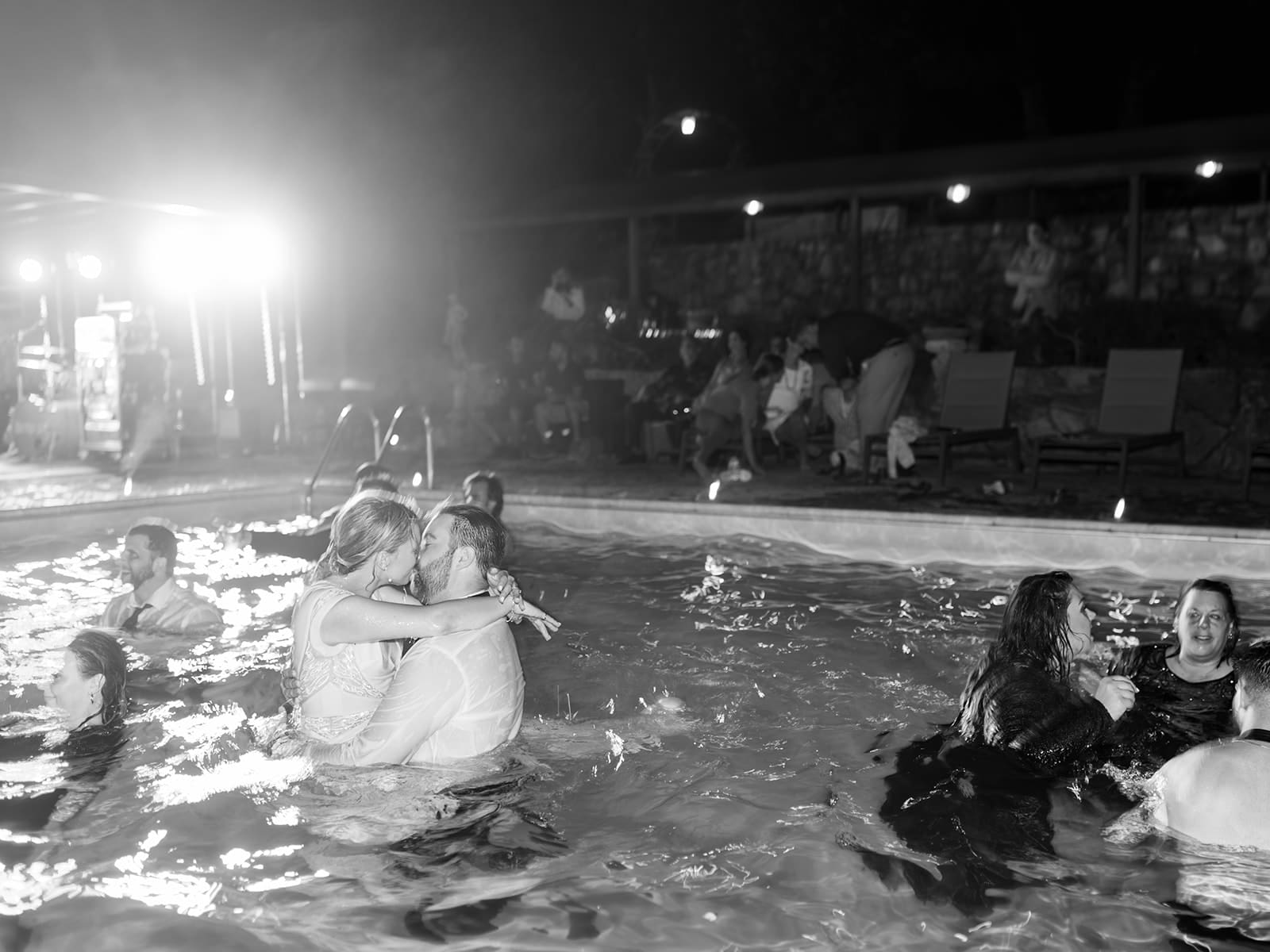 Black and white photo of a bride and groom kissing after they had jumped into a pool together