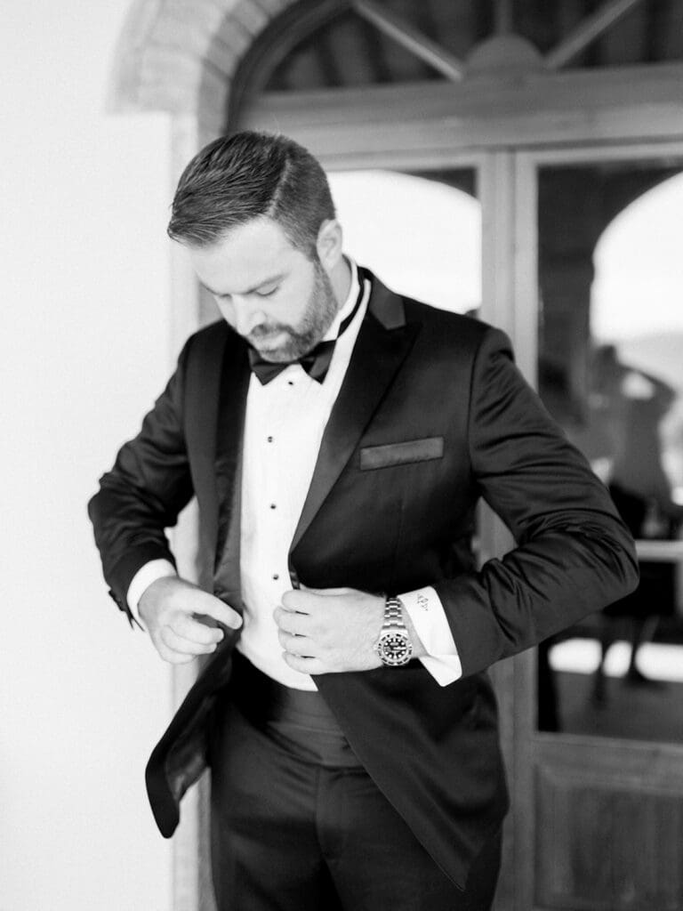 Black and white photo of a groom buttoning up his suit for his summer wedding in Tuscany, Italy at Villa Petra