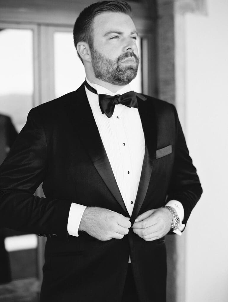 Black and white photo of a groom buttoning up his suit for his summer wedding in Tuscany, Italy at Villa Petra