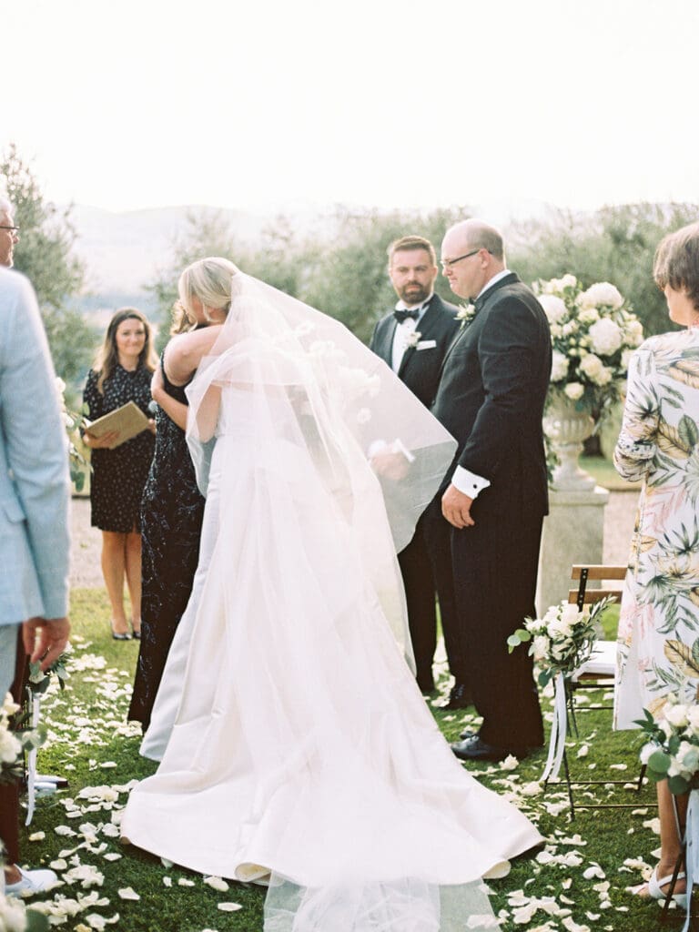 Brides parents hugging her as she meets her groom at the alter. 