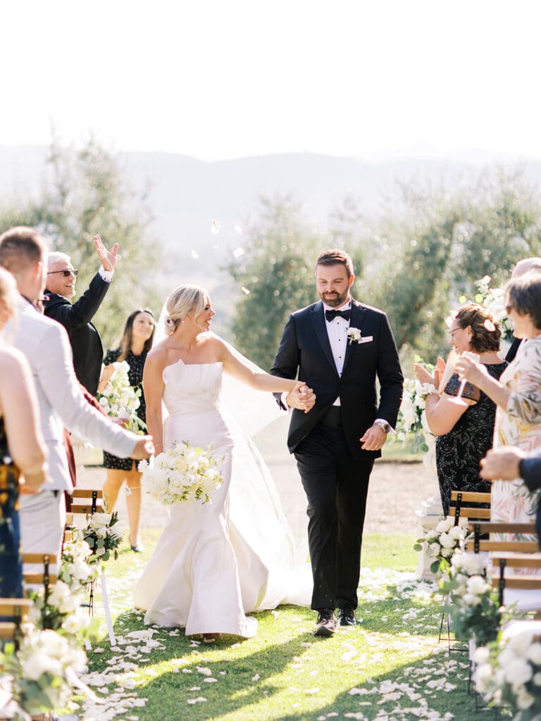 Bride and groom walking down the aisle during their outdoor summer wedding ceremony at Villa Petrea in the hills of Tuscany, Italy.