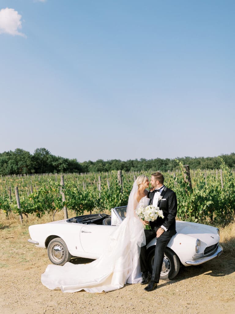 Bride and grooms outdoor summer wedding portraits with a classic white car in the hills of Tuscany, Italy.