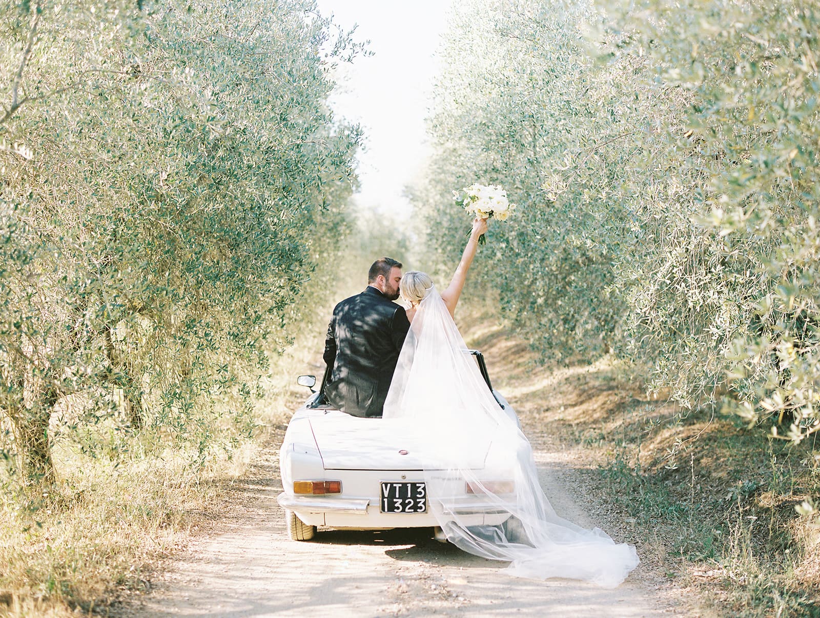 Bride and groom riding in a classic white car on a first road in Tuscany, Italy.