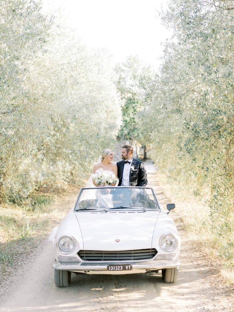 Bride and groom riding in a classic white car on a first road in Tuscany, Italy.