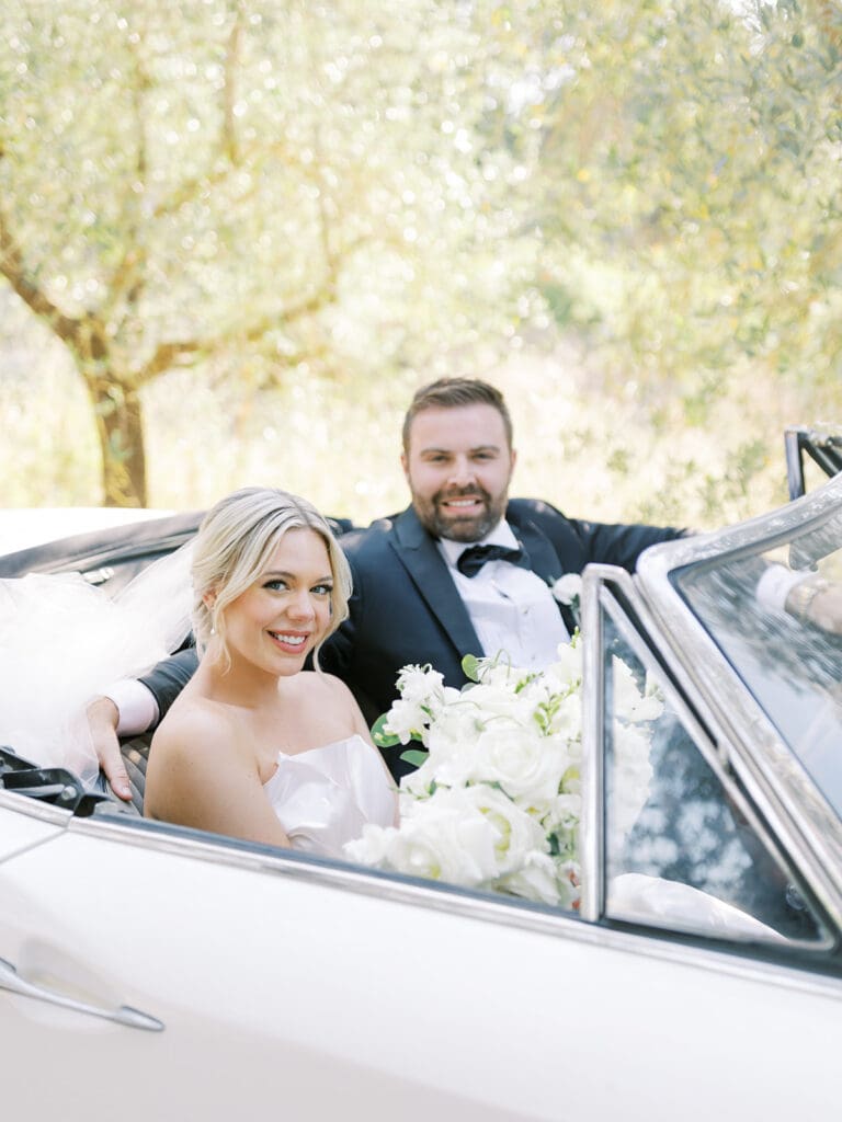 Bride and groom riding in a classic white car on a first road in Tuscany, Italy.