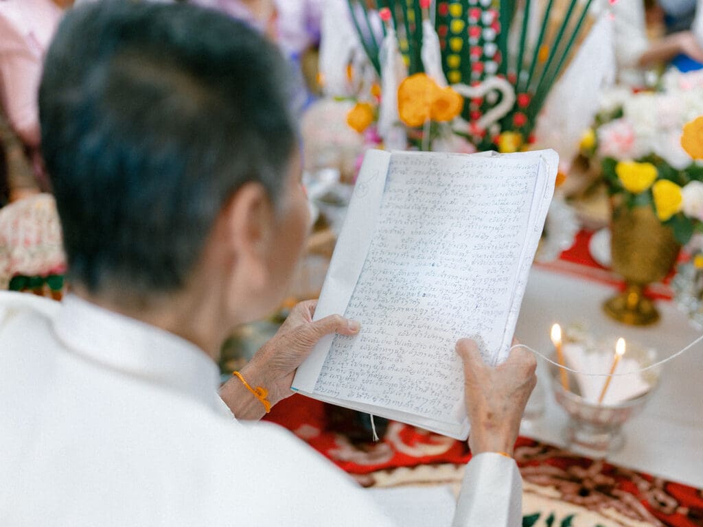 Elder of the family reading during a at-home Lao and Vietnamese wedding ceremony