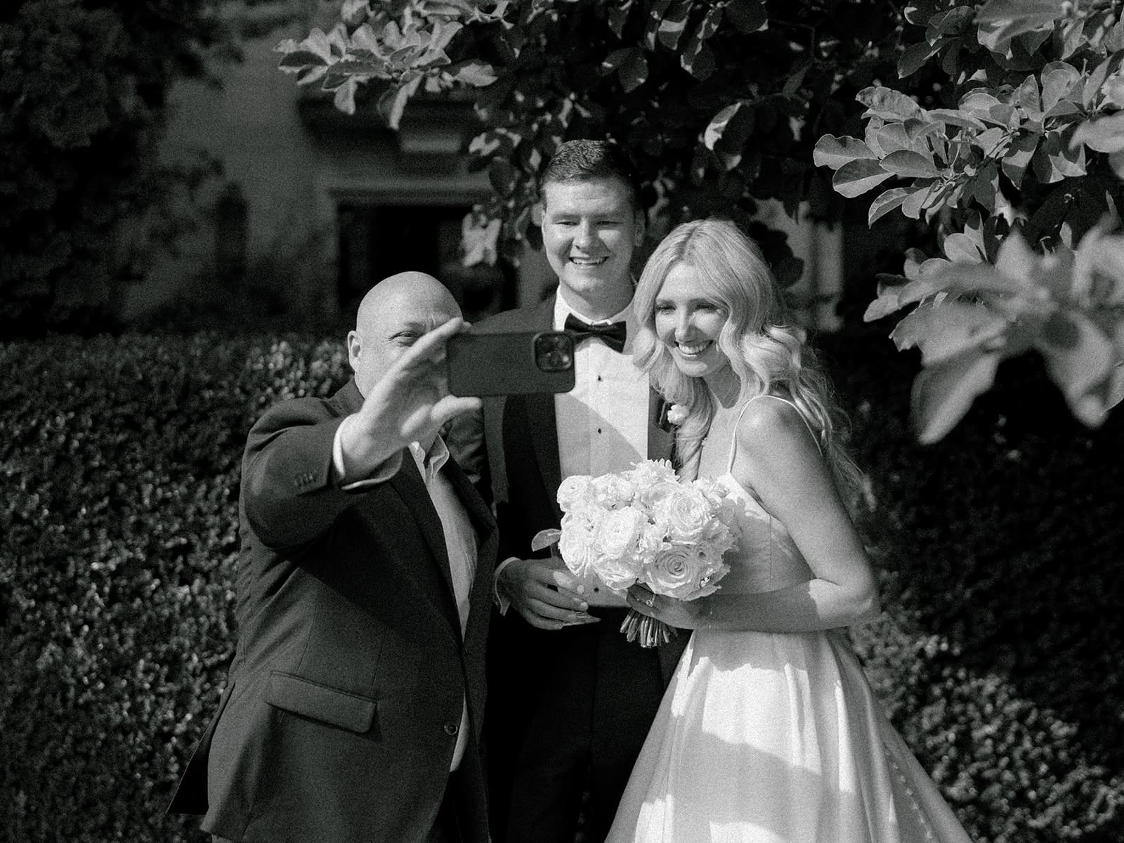 Black and white photo of bride and groom taking a selfie with a wedding guest