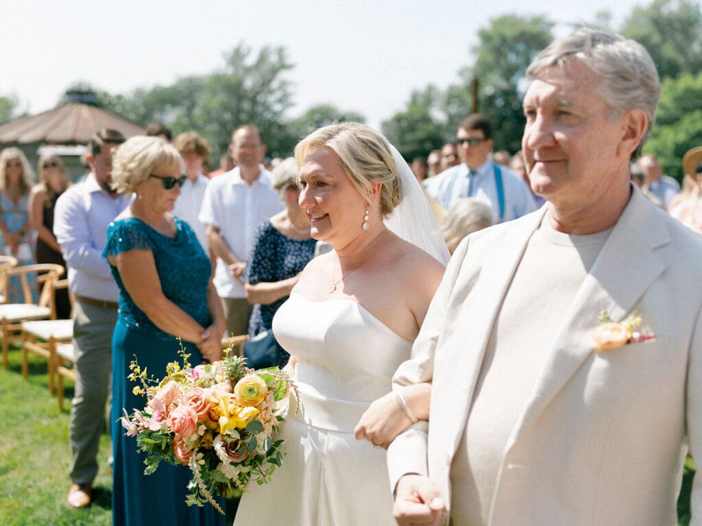 Bride being walked down the aisle by her father during their Journeyman Distillery wedding ceremony in Three Oaks, Michigan