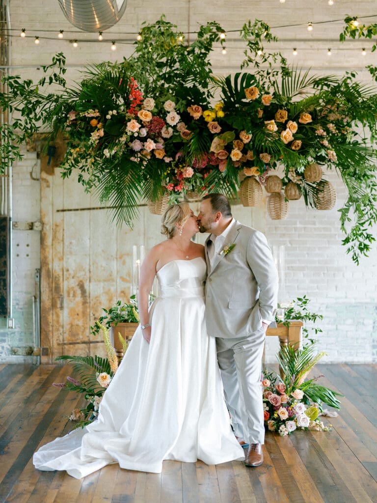 Bride and groom kissing in front of their sweethearts table at Journeyman Distillery wedding venue in Three Oaks, Michigan
