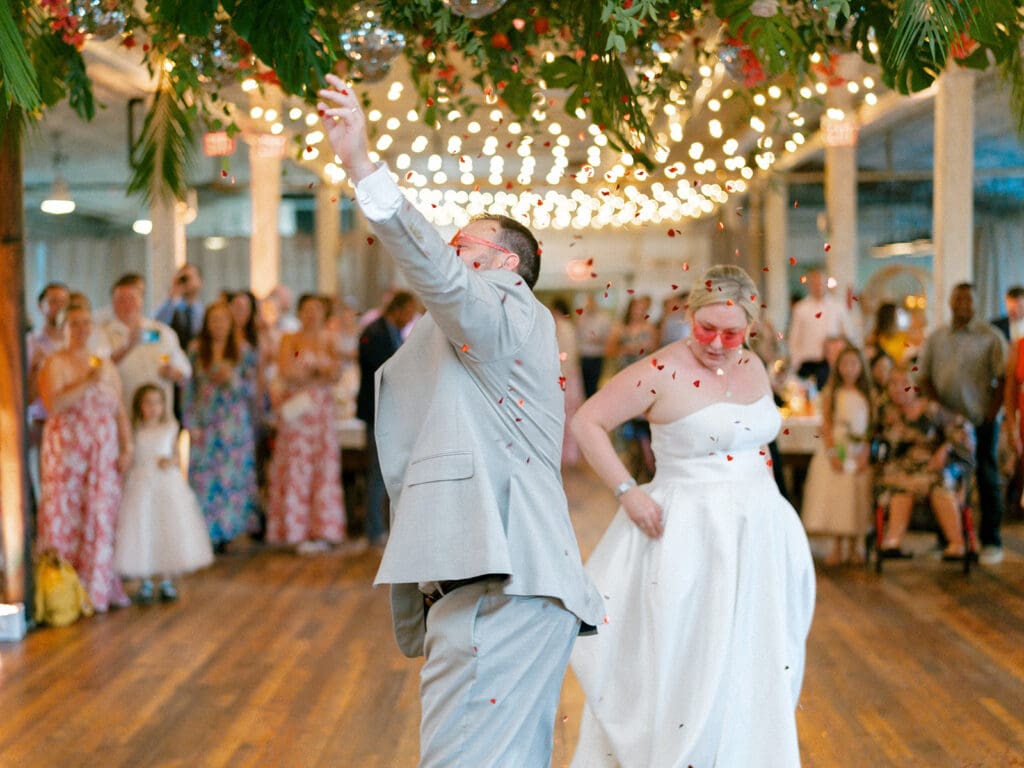 Bride and groom wearing heart sunglasses and sharing their first dance while confetti is dropping down on them