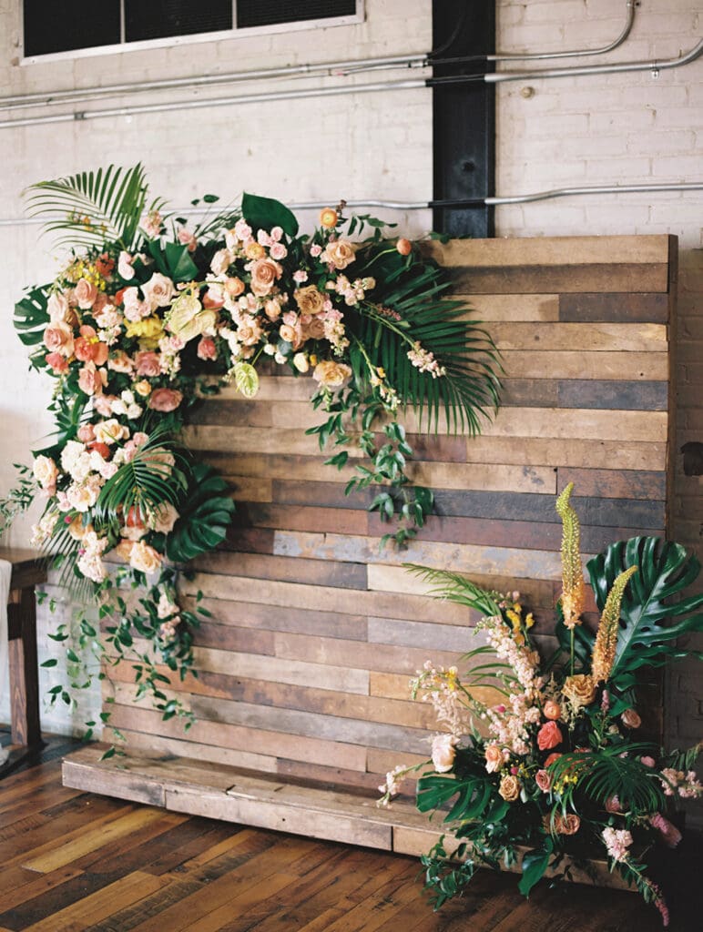 A wedding reception backdrop piece with lush florals and tropical leaves