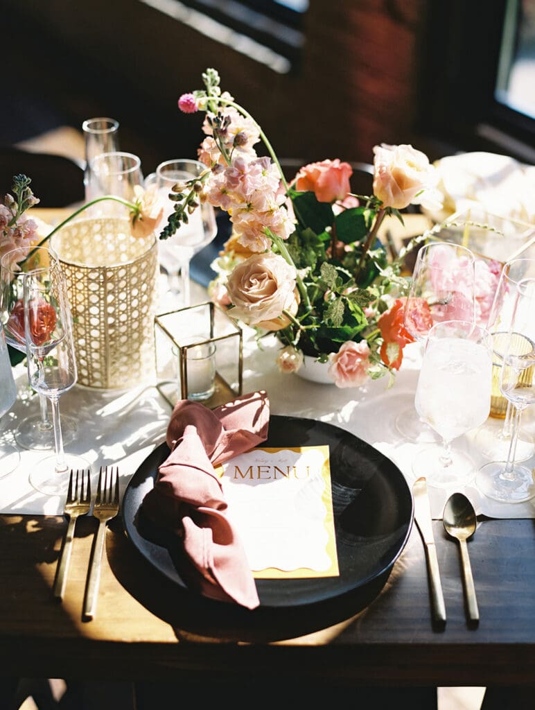 An elegant table setting with modern black plates, custom yellow menus, and gold flatware.