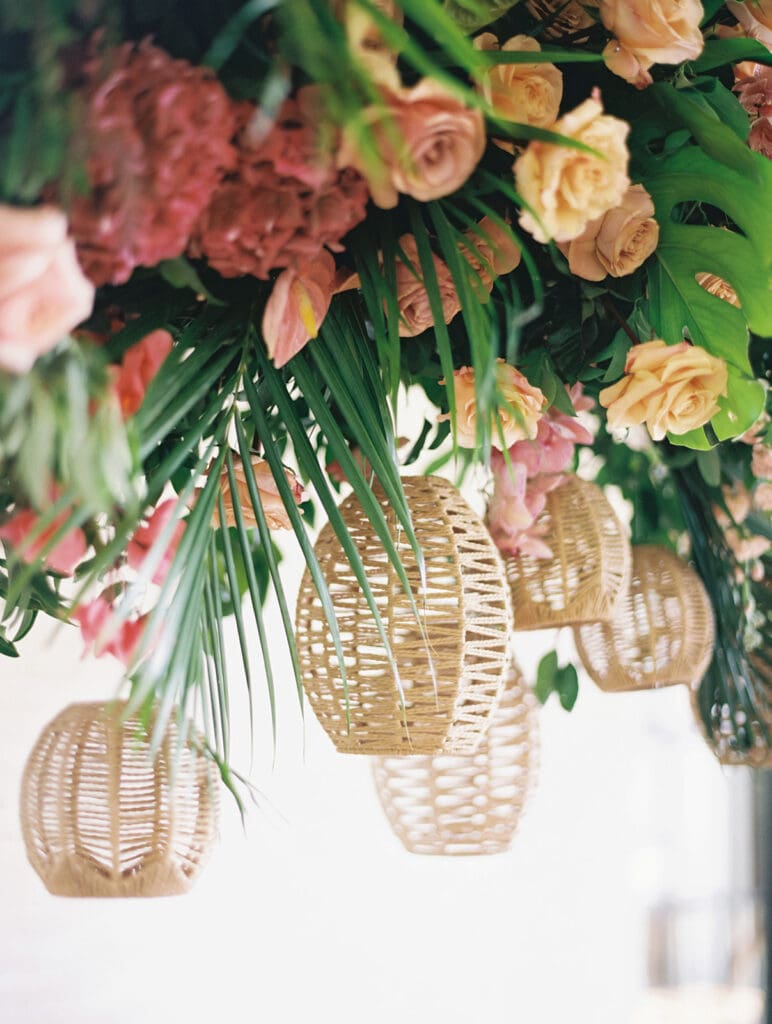 Hanger wicker lanterns on a lush tropical floral installation for a wedding reception