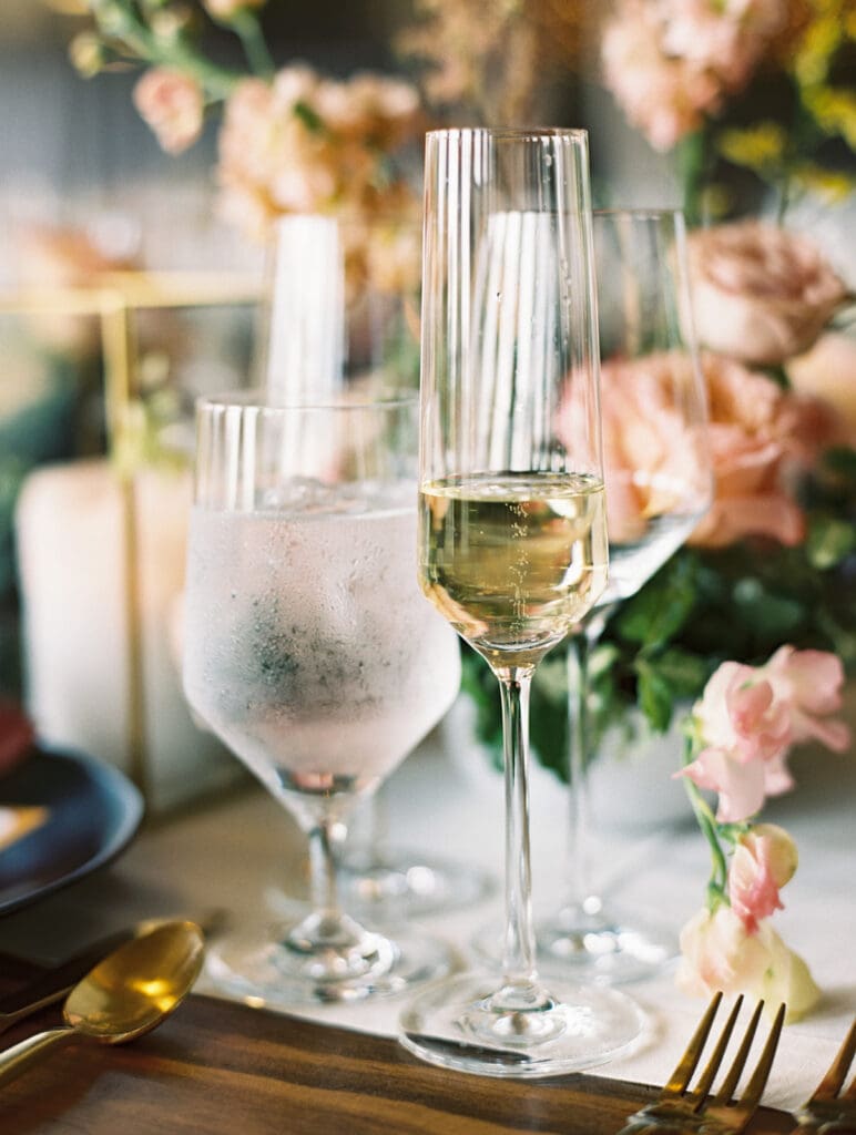 Wedding reception detail shot with champagne, water, gold flatware, and florals