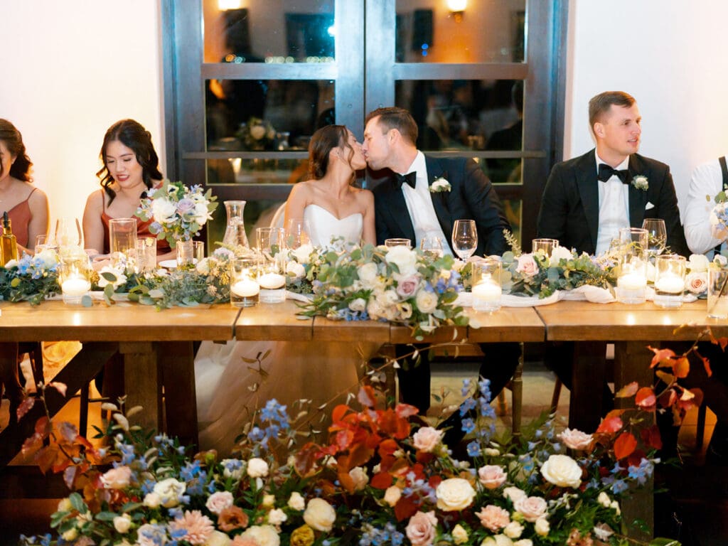 Bride and groom kissing at their head reception table