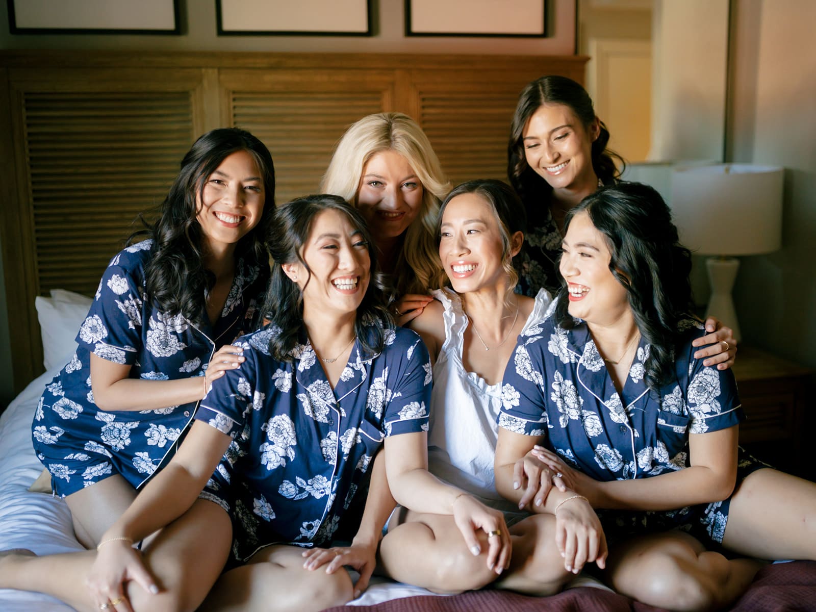 Bride and her bridesmaids sitting on a bed and posing for photos