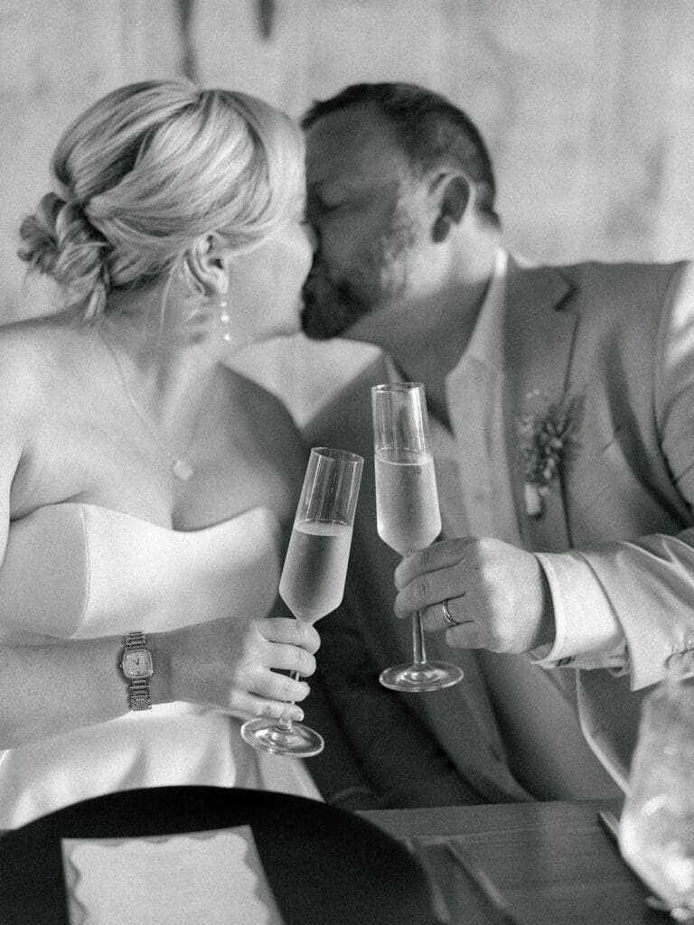 Black and white photo of a bride and groom toasting their champagne at their sweethearts table