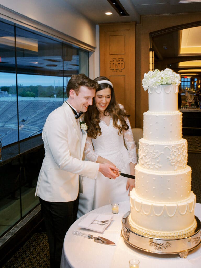 Bride and groom cutting into their classic white five-tiered wedding cake
