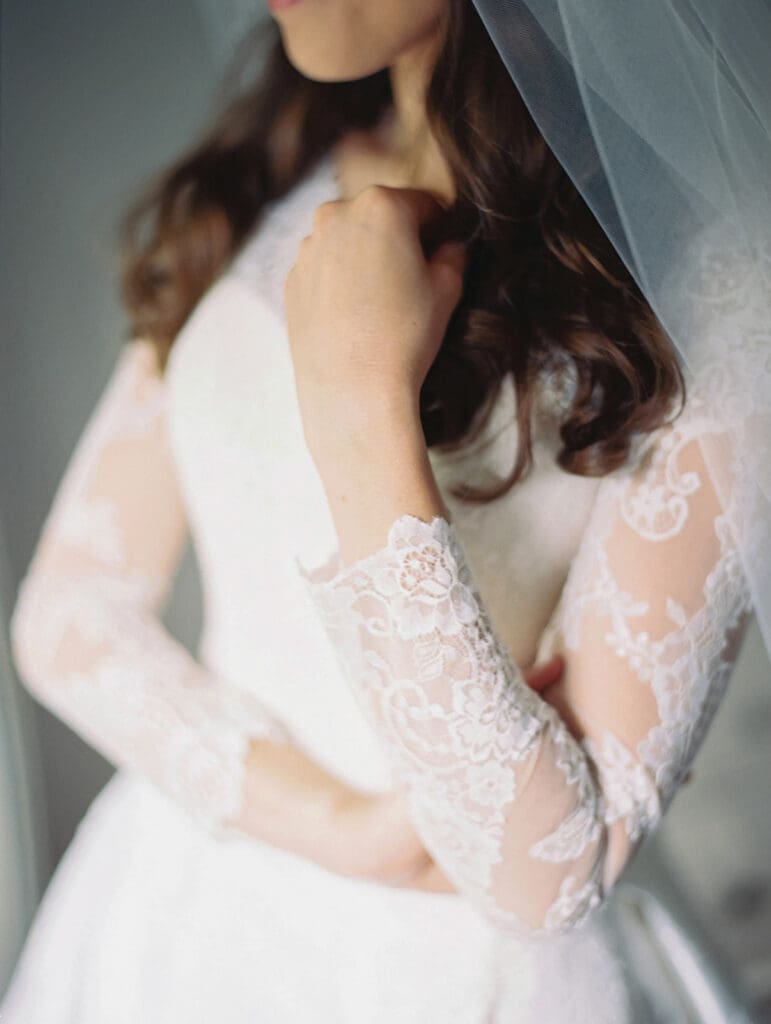 Close up detail shot of a bride wearing her long sleeved wedding dress with her hair down and a veil. 