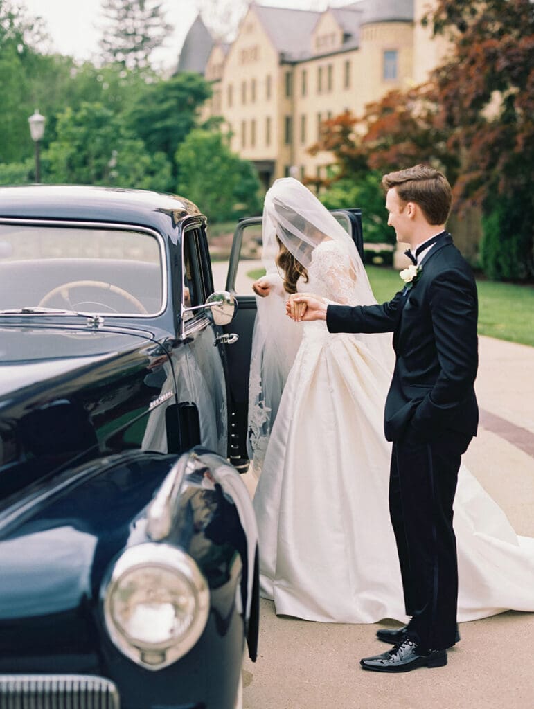 Groom helping his bride get into their vintage car