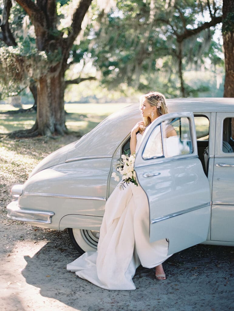 Bride posing with a classic car for her Middleton Place wedding portraits