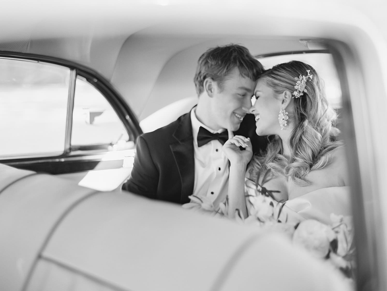 Black and white photo of a bride and groom in a classic white car